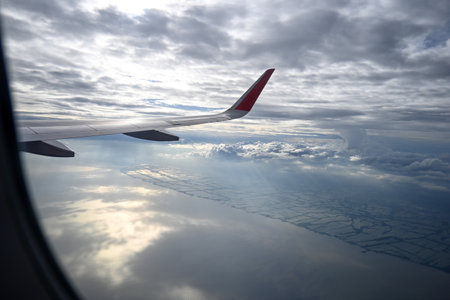 Captivating aerial view from an airplane wing, showcasing a dramatic cloudscape over a serene coastal landscape under soft lighting, perfect for travel imagery.の写真素材