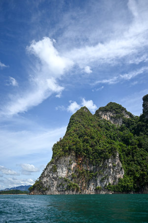 A stunning view of a towering rocky cliff draped in vibrant greenery, set against a bright blue sky...