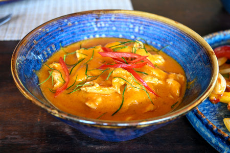 Indulge in a rich coconut chicken curry served in a beautiful blue bowl. This dish features fresh...