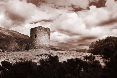Ruin of a castle consisting of a single tower in the mountains in sepia colour and a dramatic skyの写真素材