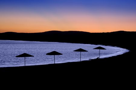 Silhouettes of grass top beach umbrellas at sunset on a Greek islandの写真素材