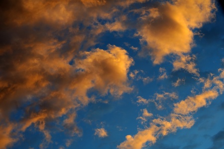 Dramatic warm colored clouds moments before dusk against blue skyの写真素材