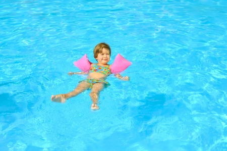 Smiling toddler girl learning to swimm in the swimming poolの写真素材