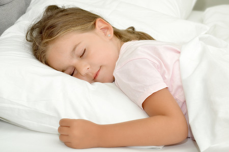 Adorable little girl sleeping in a bedの写真素材