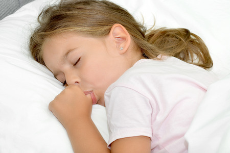 Adorable little girl sleeping in a bedの写真素材