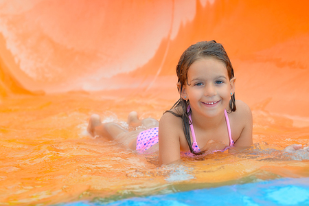 Real toddler girl enjoying her summer vacation on water slide at aquapark