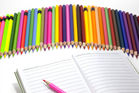 Various color pencils over  blank notepad . Isolated on white backgroundの写真素材