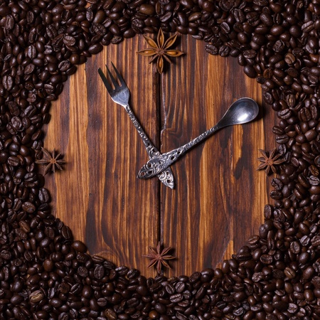 Clock made of coffee, teaspoon, dessert fork and anise on dark wooden background