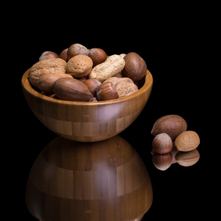 Nuts in wooden bowl on a mirror  Isolated on black 