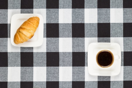 Cup of coffee and croissant on black and white checkered tablecloth の写真素材