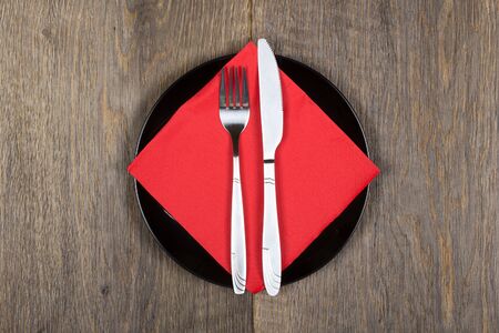 Fork, knife and red napkin on black plate  Wooden background の写真素材