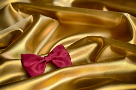 Red bow tie on draped golden satinの写真素材
