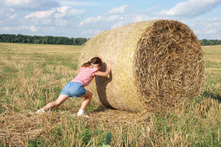 child pushes a bale of hayの写真素材