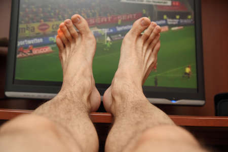 feet on the background of the TV showing footballの写真素材