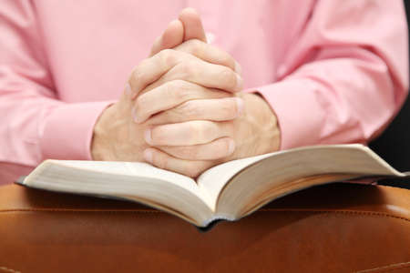 man folded his hands in prayer on the Bible