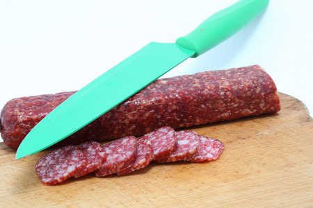 sliced sausage and knife isolated on whiteの写真素材