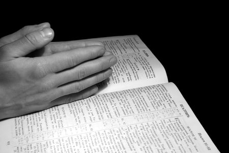 A mans hands clasped in prayer over a  Bible