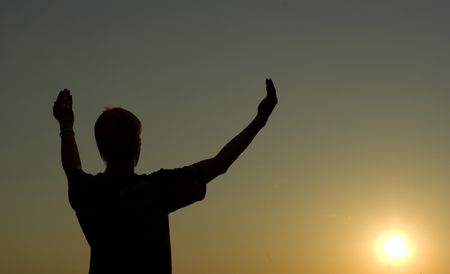 A man stands on against a sun with heaved up hands      