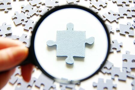 Hand with magnifying glass and puzzle isolated on white backgroundの写真素材