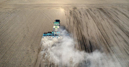 A farmer in a tractor prepares land with a sowing cultivator as part of pre-sowing work at the beginning of the spring agricultural season on agricultural land.の写真素材