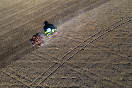A farmer in a tractor prepares land with a sowing cultivator as part of pre-sowing work at the beginning of the spring agricultural season on agricultural land.の写真素材
