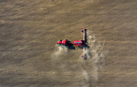 A farmer in a tractor prepares land with a sowing cultivator as part of pre-sowing work at the beginning of the spring agricultural season on agricultural land.の写真素材