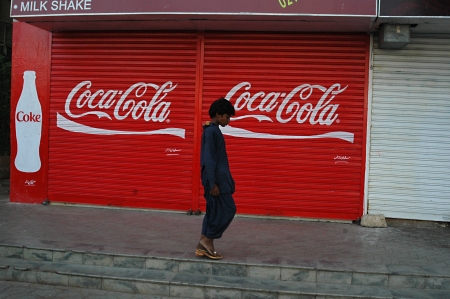 KARACHI/PAKISTAN_   Pakistani males pass by closed shop coke or coca cola commercial at shop door today on 4th October 2012    のeditorial素材