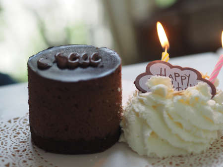 Dark Chocolate Birthday Cake piece on wooden plate candle with Whipped Cream on white paperの写真素材