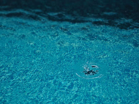 Rain drops falling blue water in pool background ripples on the surface texture, glittering bokeh abstractの写真素材