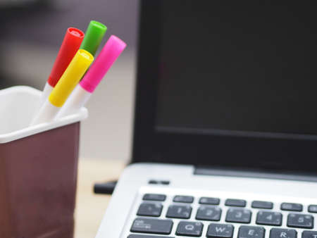 many magic pen red, pink, yellow, green color in brown plastic box, blurred of notebook background