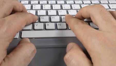 man's hands typing on a gray keyboard with white lettersの写真素材