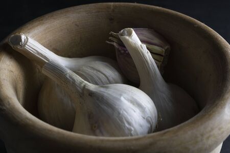 group of garlic heads in a wooden bowl with a black backgroundの写真素材