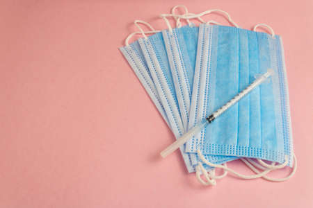 syringe and needle on a group of isolated copper masks on a pink background shifted to the rightの写真素材