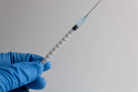 syringe with needle held by a hand protected by a blue insulated glove on a white backgroundの写真素材