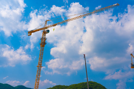 Construction cranes work on creation site against blue sky background.の写真素材