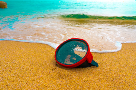 A diving mask lies on a sandy beach and is washed by waves of water