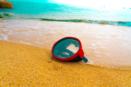 A diving mask lies on a sandy beach and is washed by waves of water