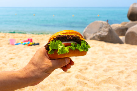Man holding burger in a hand against beach backgroundの写真素材