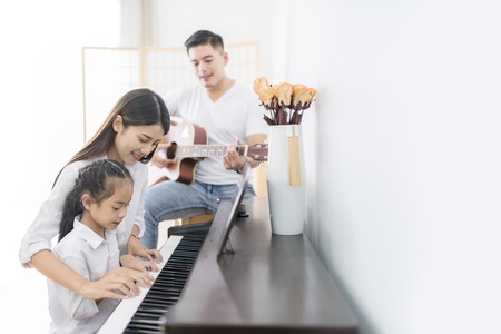 Asian family, mother  and daughter playing Piano,father playing guitar in family band at home, concept for family relationshipの写真素材