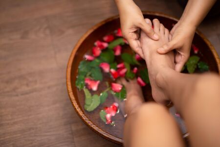 Top View shot of a woman feet dipped in water with petals in a wooden bowl. Beautiful female feet at spa salon on pedicure procedure.の写真素材