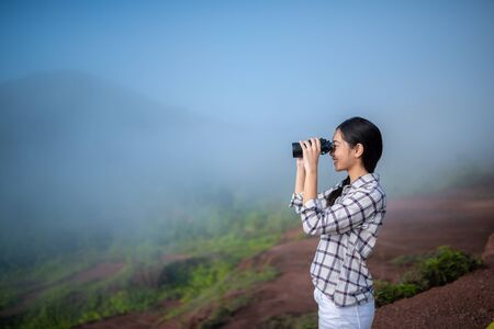 Young asian traveler looking through binoculars mountain backgroundの写真素材