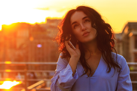 beautiful brunette talking on the phone at sunsetの写真素材