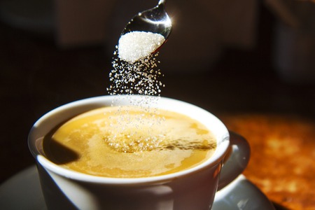 sugar from a spoon flies in a cup of coffeeの写真素材