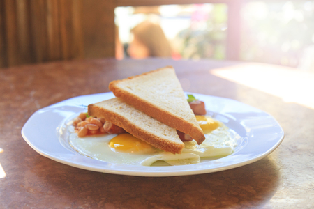 egg with beans and toast on a white plate with sunny hotspotの写真素材