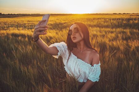 beautiful girl takes a selfie in a rye field at sunsetの写真素材