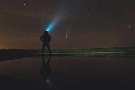 guy in the hood shines a lantern up and looks at the comet Neowiseの写真素材