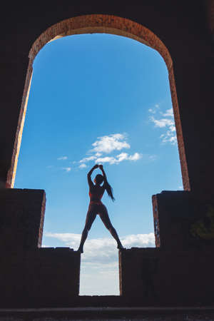 girl stands in a huge arch with her hands raised up