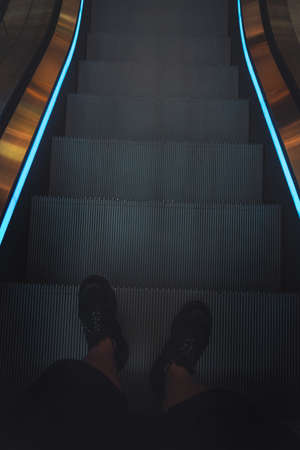 legs of a man in black sneakers on an escalator