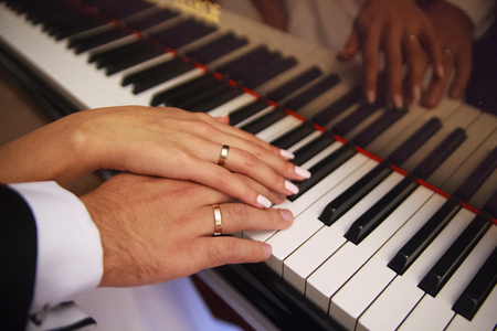 Two hands on the piano. Play. The piano keys. Wedding. A touch of hands. Wedding rings. Closeupの写真素材