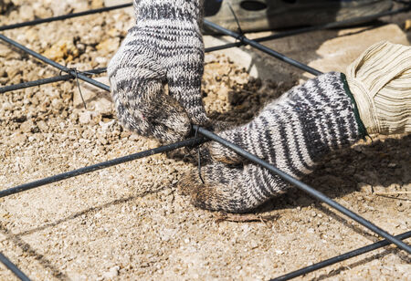 Authentic construction worker installing binding steel wires to reinforcement steel bars in construction site. の写真素材
